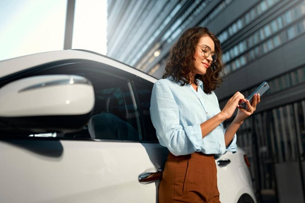 Renter checking a phone beside a parked car while choosing a listing